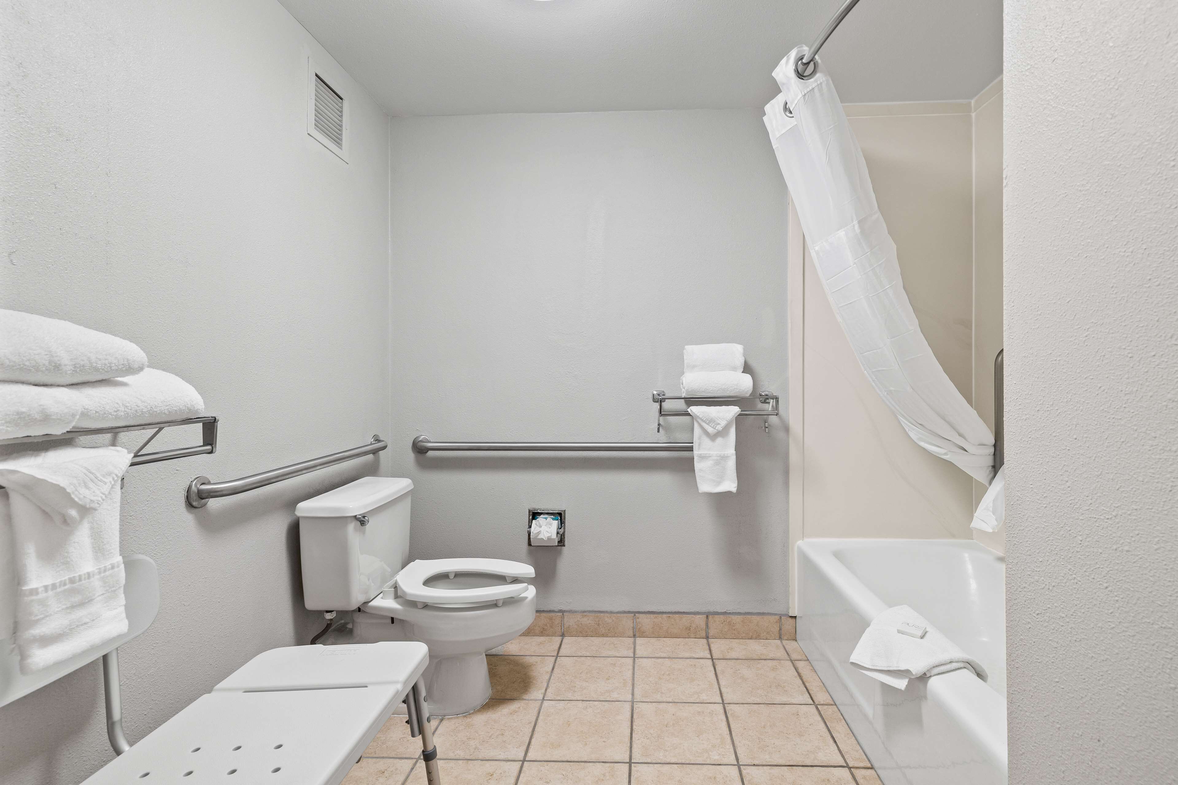 Un baño pequeño y blanco con inodoro, lavamanos, ducha con cortina y barra de apoyo.