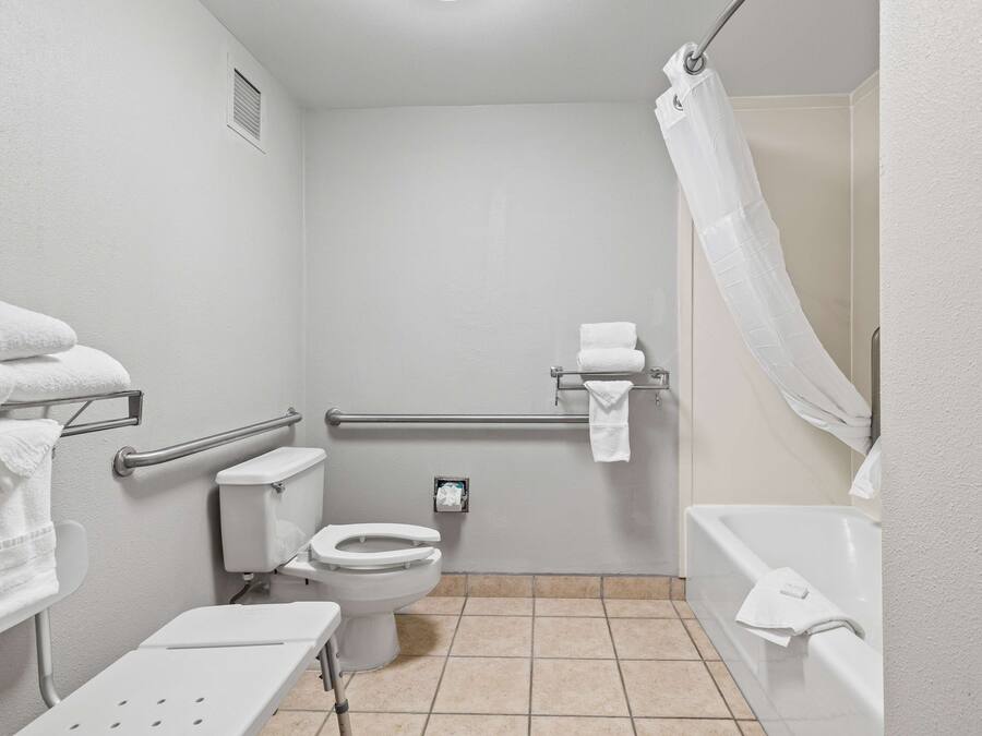 A small, white bathroom with a toilet, a sink, a shower with a curtain, and a grab bar.