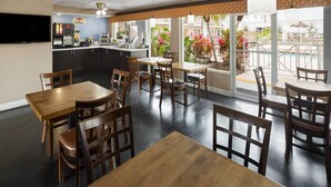 Un restaurante con mesas y sillas de madera, una zona de cocina y vistas a una piscina.