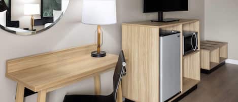 A hotel room with a wooden desk, a black chair, a television, a mirror, and a cabinet with a microwave.