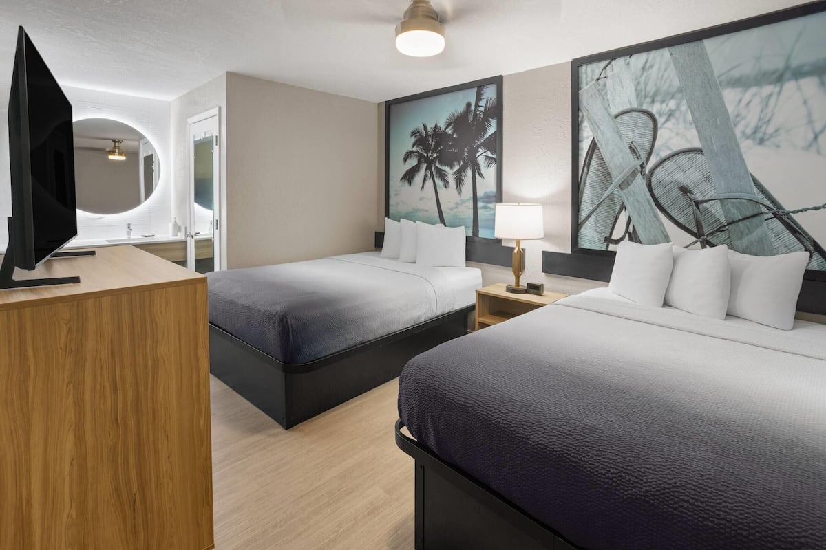 A hotel room with two beds, a TV, a mirror, and artwork on the wall.