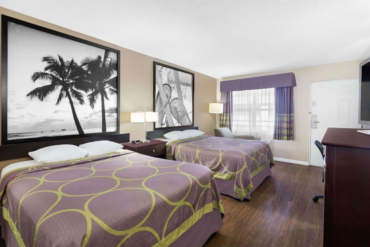 A hotel room with two beds, a desk, a chair, a TV, and artwork on the walls.