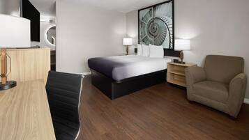 A modern hotel room with a bed, a desk, a chair, a sofa, and a large wall art piece.