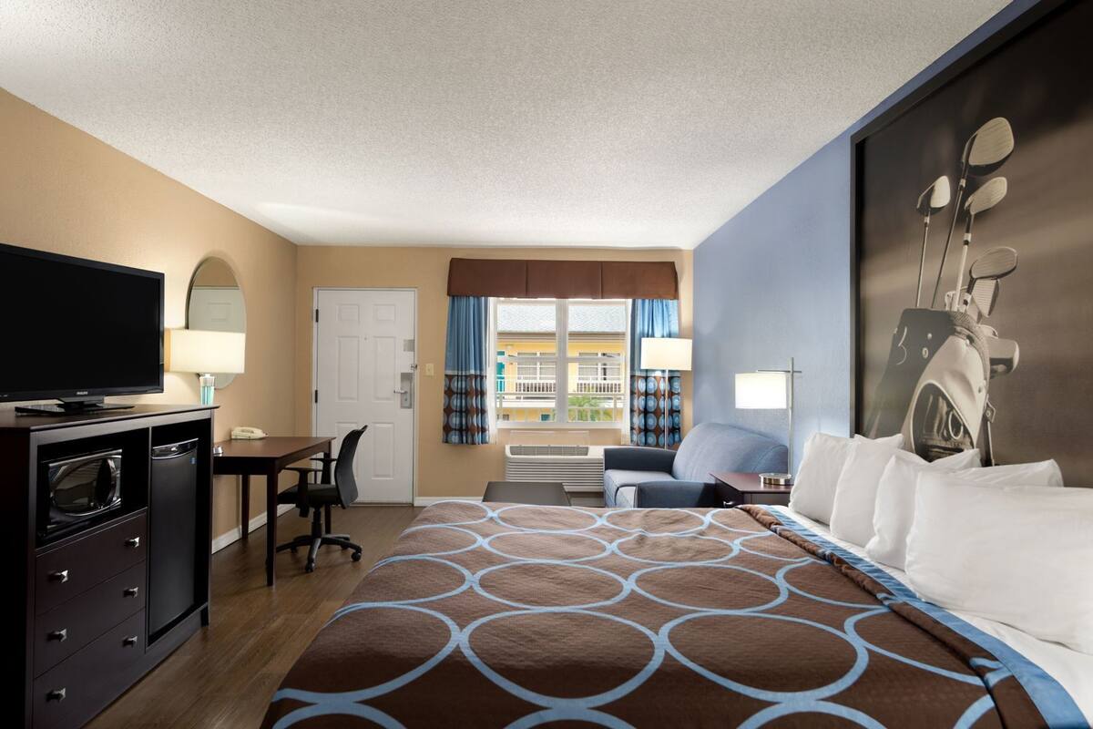 A hotel room with a bed, desk, TV, and a view of the outside.