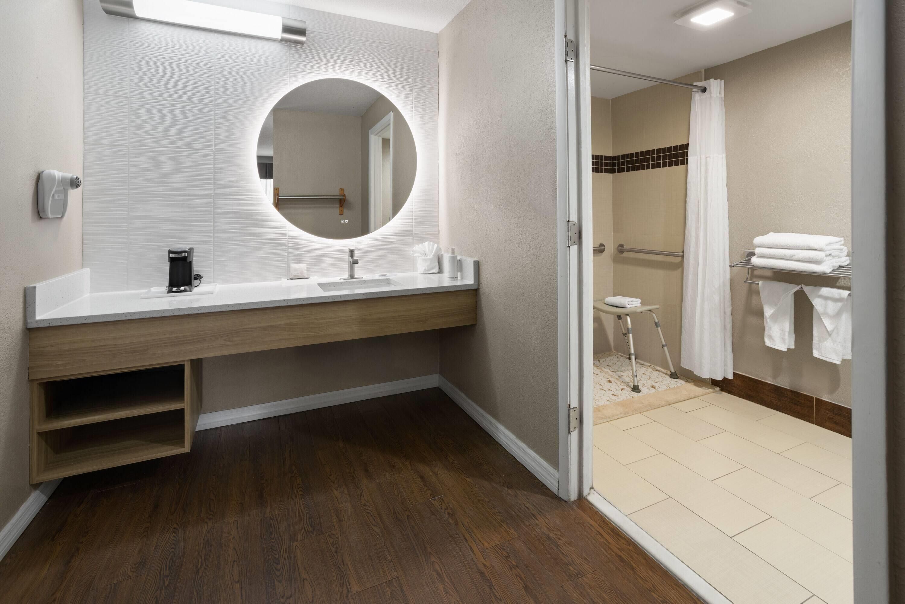 A modern bathroom with a wooden vanity, a round mirror, a shower area, and a toilet.