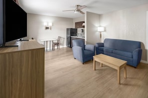 A modern living room with a flat-screen TV, a blue sofa, a wooden coffee table, and a kitchen area in the background. - Super 8 by Wyndham Ellenton Bradenton Area (Ellenton)