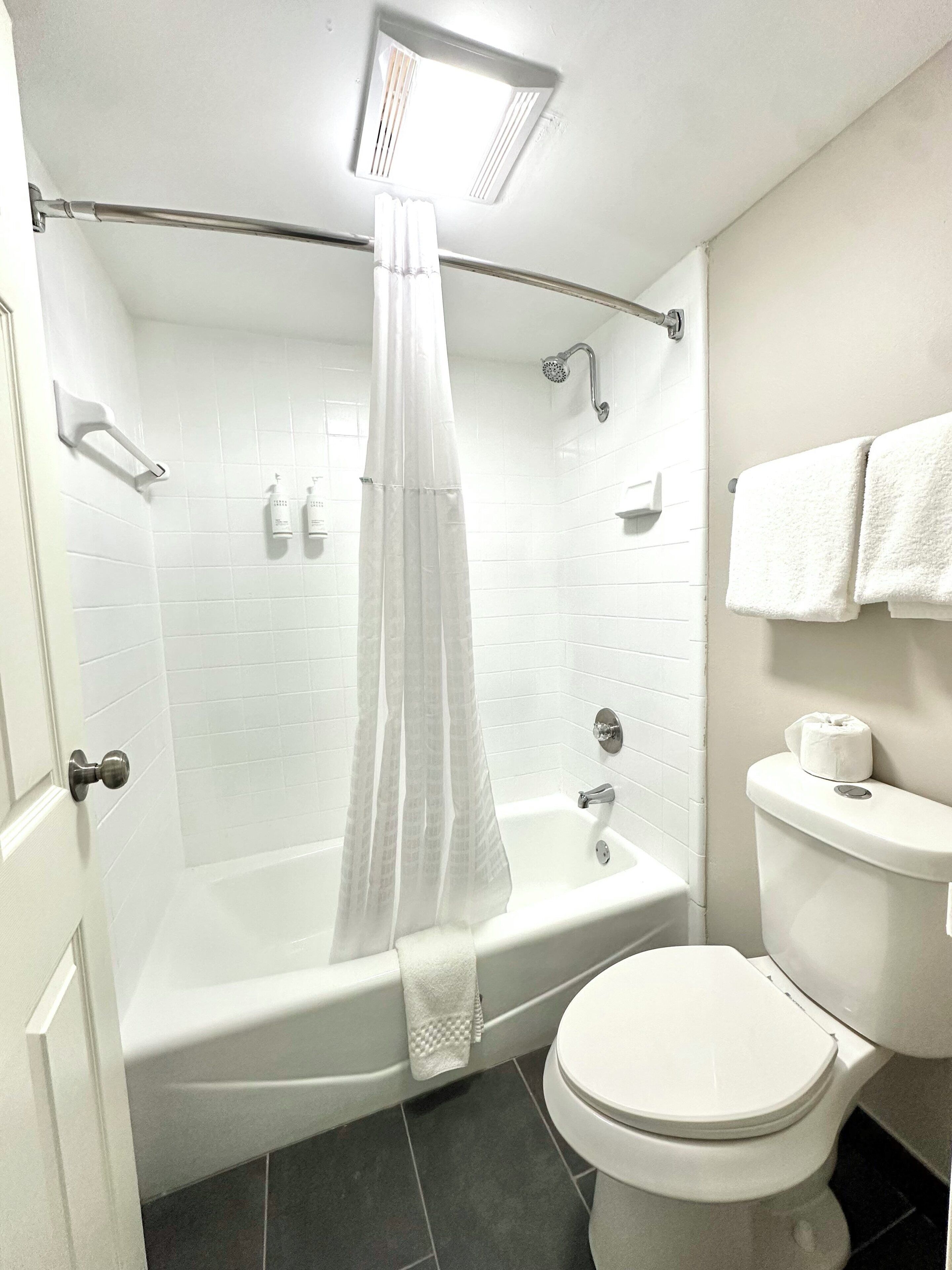 Een moderne badkamer met een badkuip, douche, toilet en een handdoekrek.