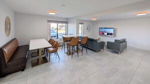 Ein modernes Wohnzimmer mit Essbereich, einer Couch, einem an der Wand montierten Fernseher und einem großen Fenster mit Außenblick.
