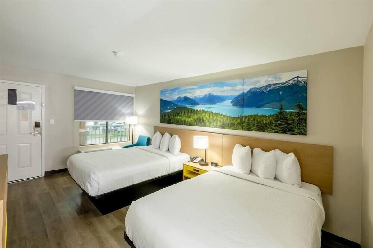 Ein Hotelzimmer mit zwei Betten, einem großen Fenster, einem Gemälde einer Berglandschaft und einer Tür.