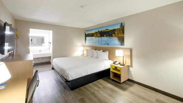 Ein Hotelzimmer mit Bett, Nachttisch, Lampe und einem Gemälde eines Sees.