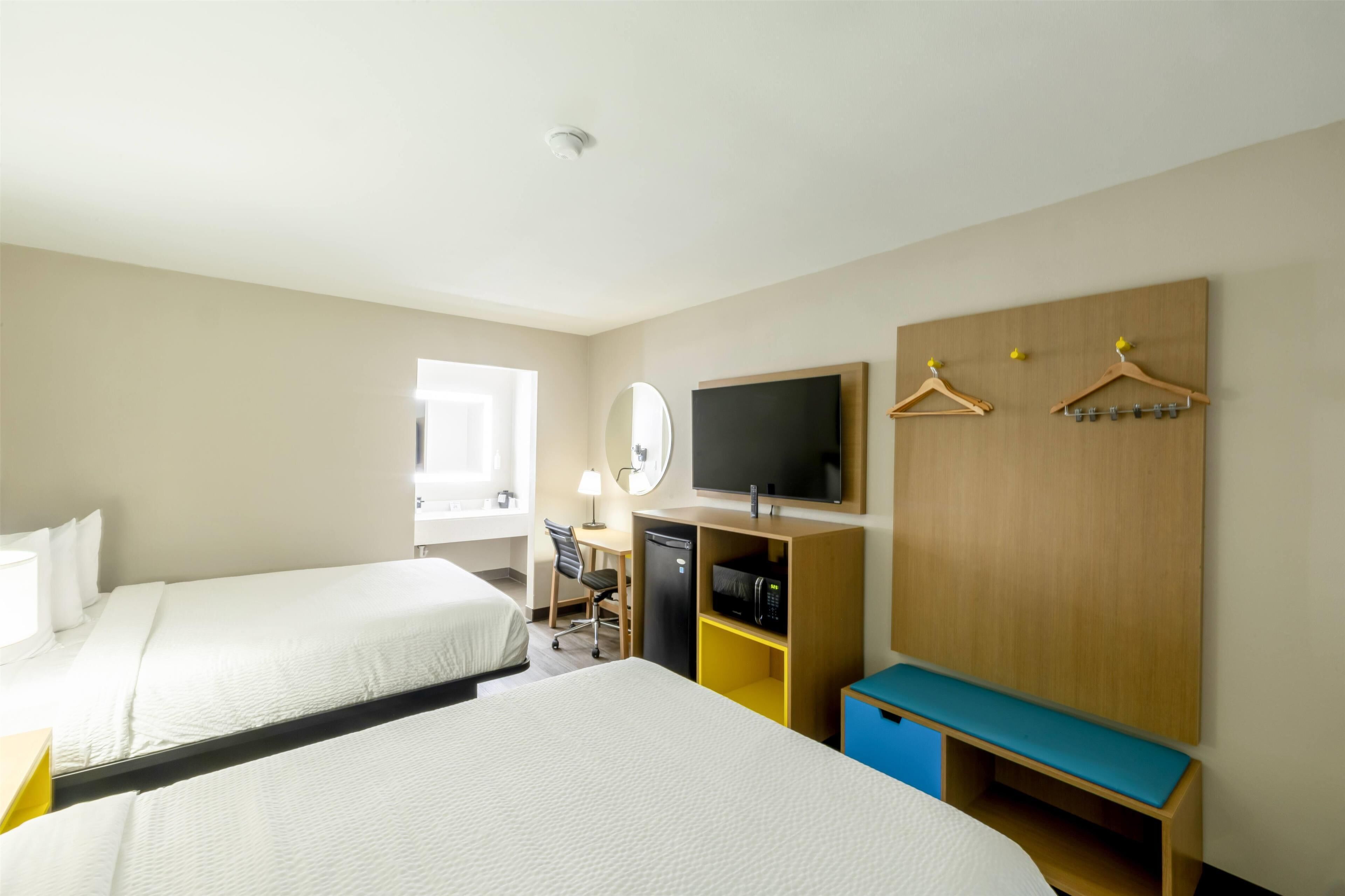 A hotel room with two beds, a desk with a chair, a television, a microwave, and a wardrobe with hangers.