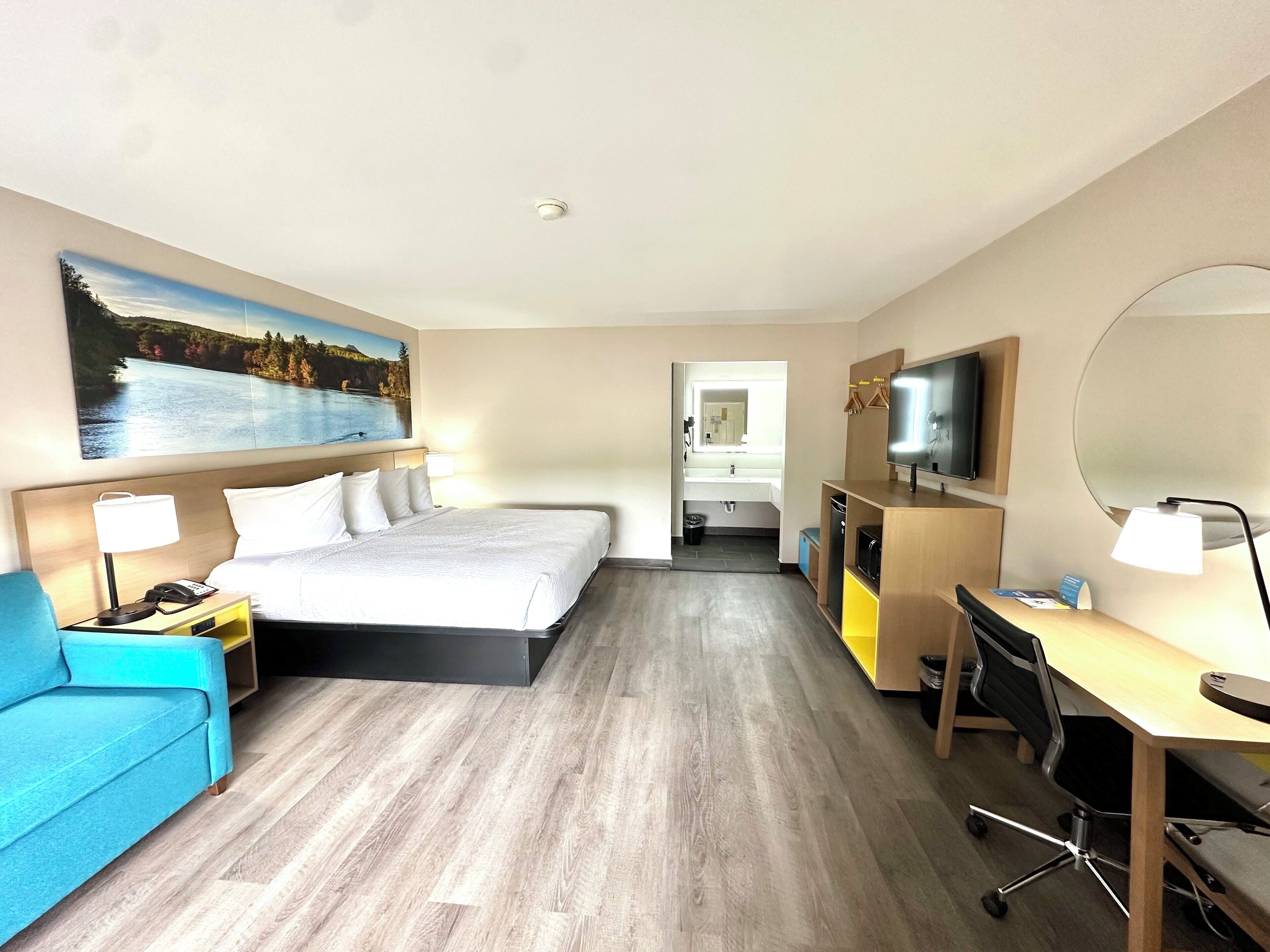A hotel room with a bed, a desk, a chair, a TV, and a painting on the wall.