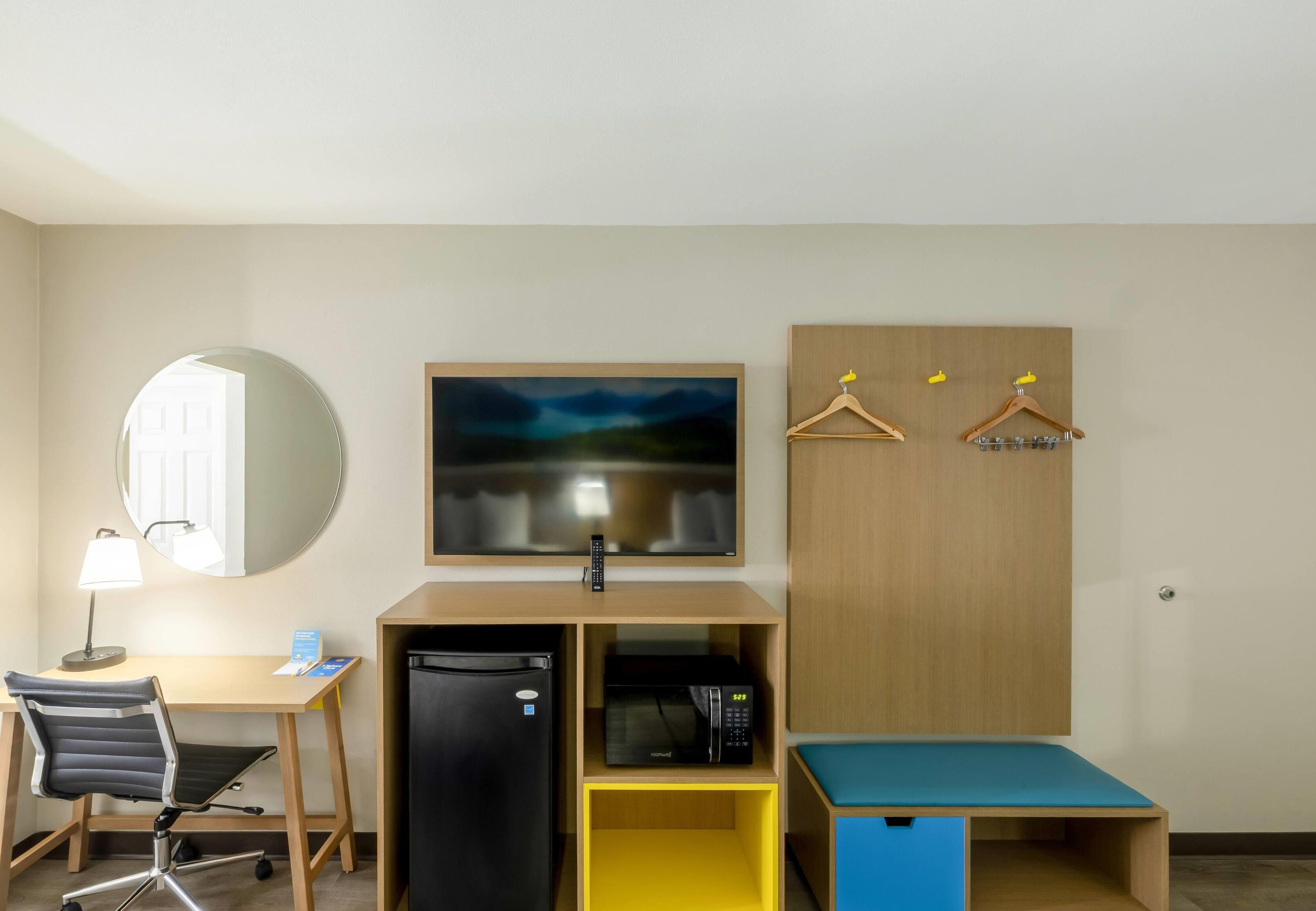 A hotel room with a desk, chair, refrigerator, microwave, and a bed with a blue mattress.