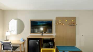 A hotel room with a desk, chair, refrigerator, microwave, and a bed with a blue mattress.