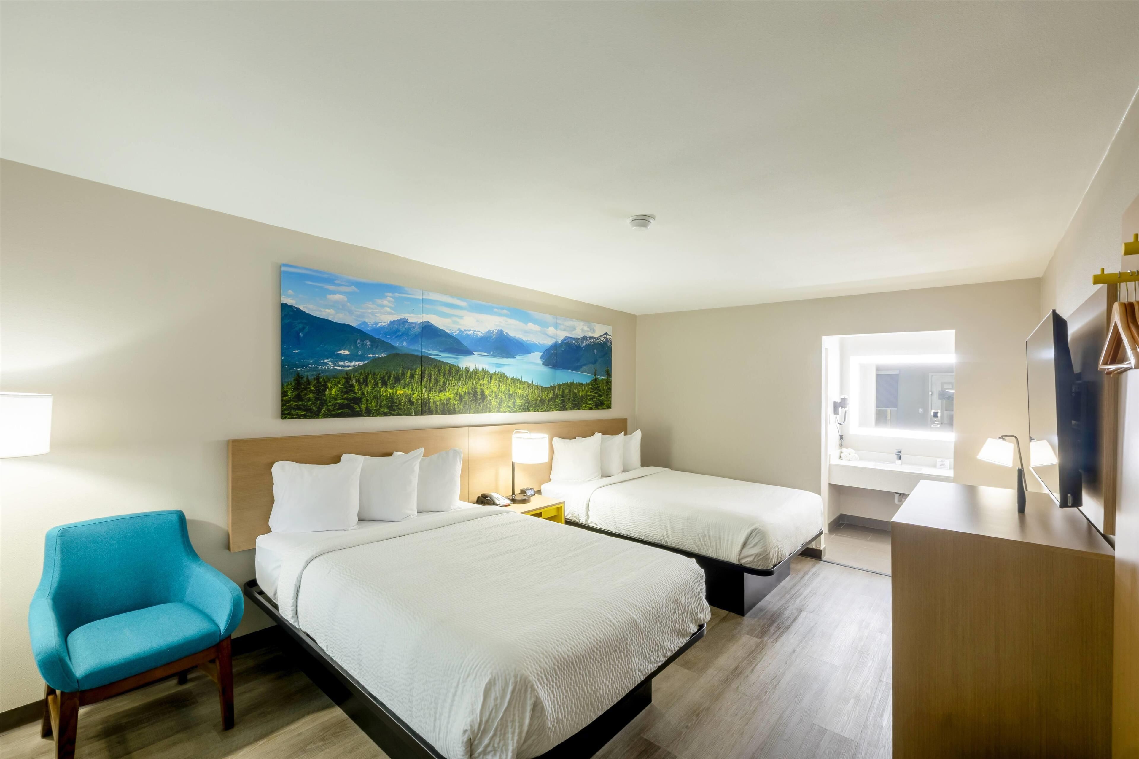A hotel room with two beds, a desk, a chair, and a large landscape painting on the wall.