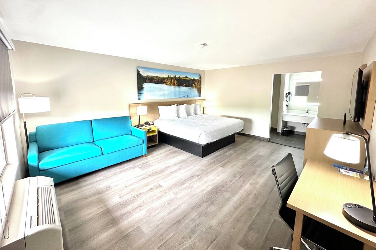 Ein Hotelzimmer mit einem Bett, einem blauen Sofa, einem Schreibtisch mit einer Lampe und einem Bild an der Wand.