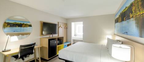 Quarto de hotel com cama, escrivaninha, cadeira, televisão e pintura de um lago.