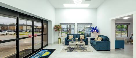 A modern lobby with a reception desk, seating area, and large windows overlooking a parking lot.