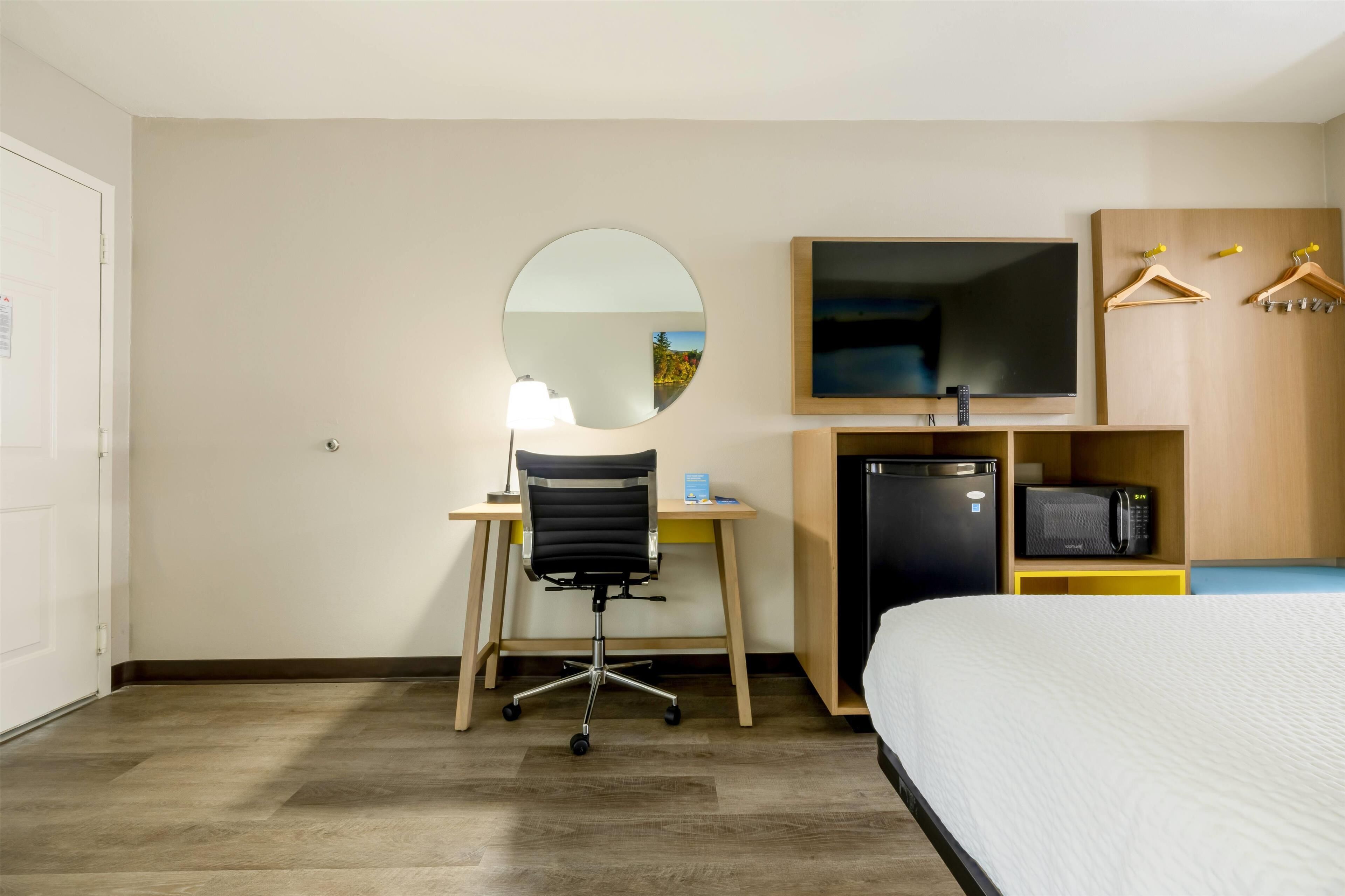 Habitación de hotel con cama, escritorio con silla, televisor, microondas y armario con perchas.