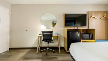 Habitación de hotel con cama, escritorio con silla, televisor, microondas y armario con perchas.