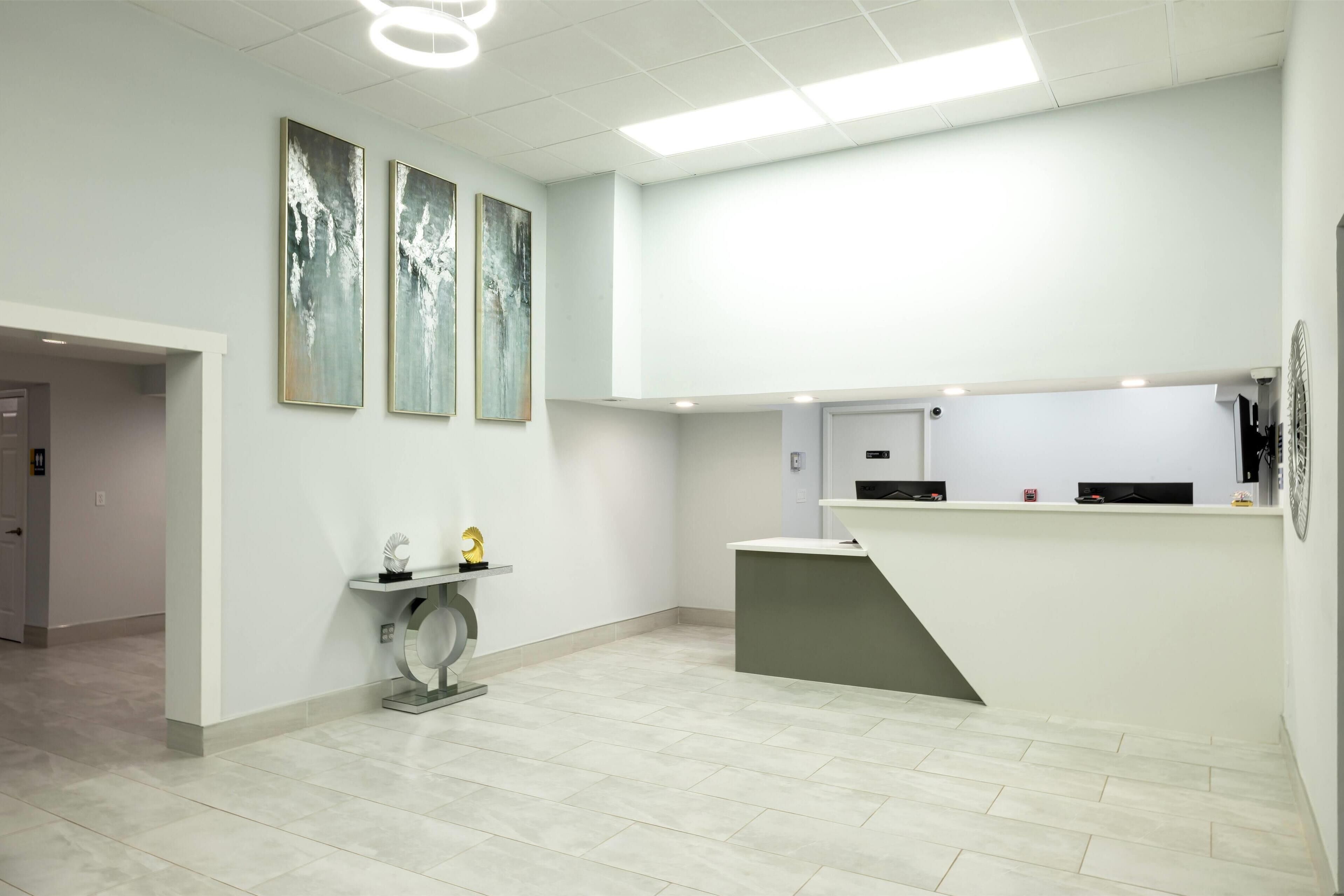 A modern reception area with a desk, a small console table, and three abstract paintings on the wall.