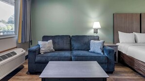 Une pièce comprenant un canapé, un lit, une table de chevet avec une lampe et une fenêtre avec des rideaux.