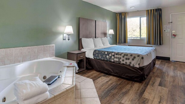 Une chambre d’hôtel avec un grand lit, une salle de bain séparée avec une baignoire et une fenêtre avec des rideaux.
