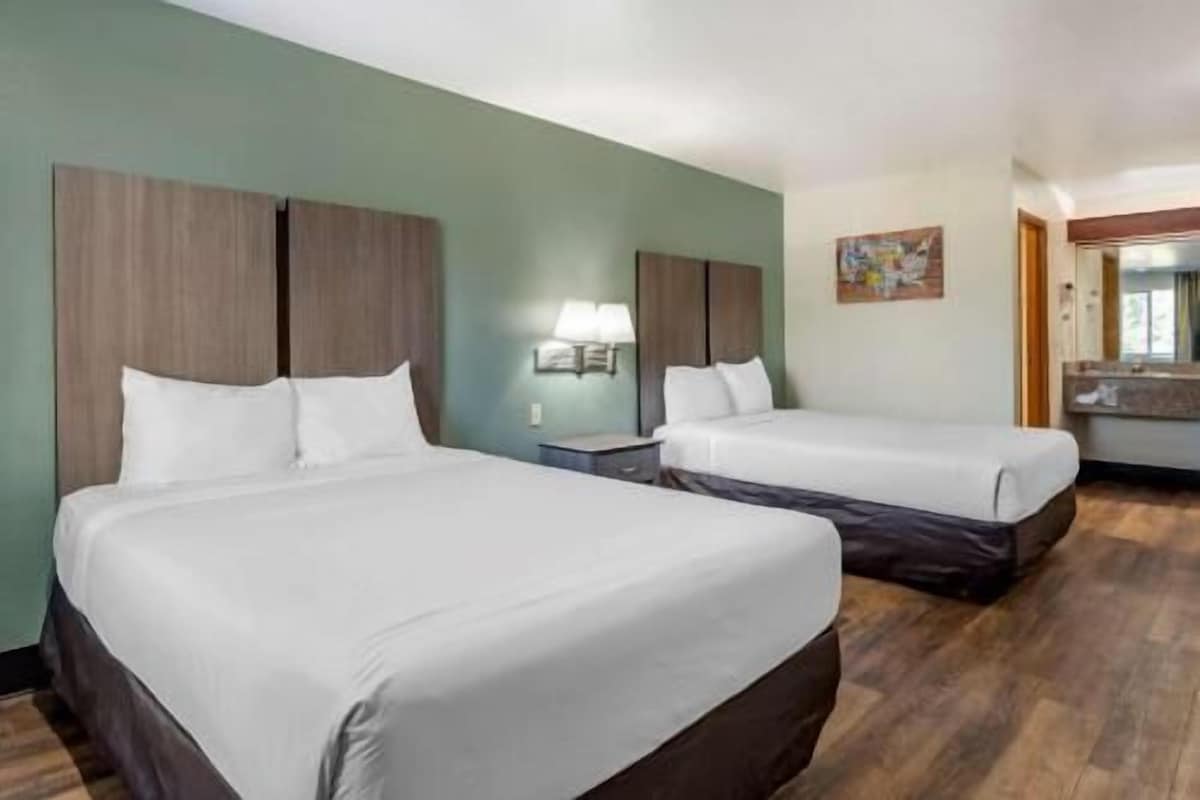 A hotel room with two beds, a nightstand, a lamp, and a painting on the wall.