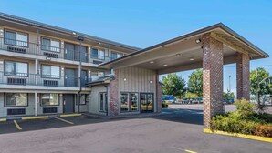 Un hôtel à plusieurs étages, doté d’une entrée couverte, d’un parking et d’un autobus visible au loin.