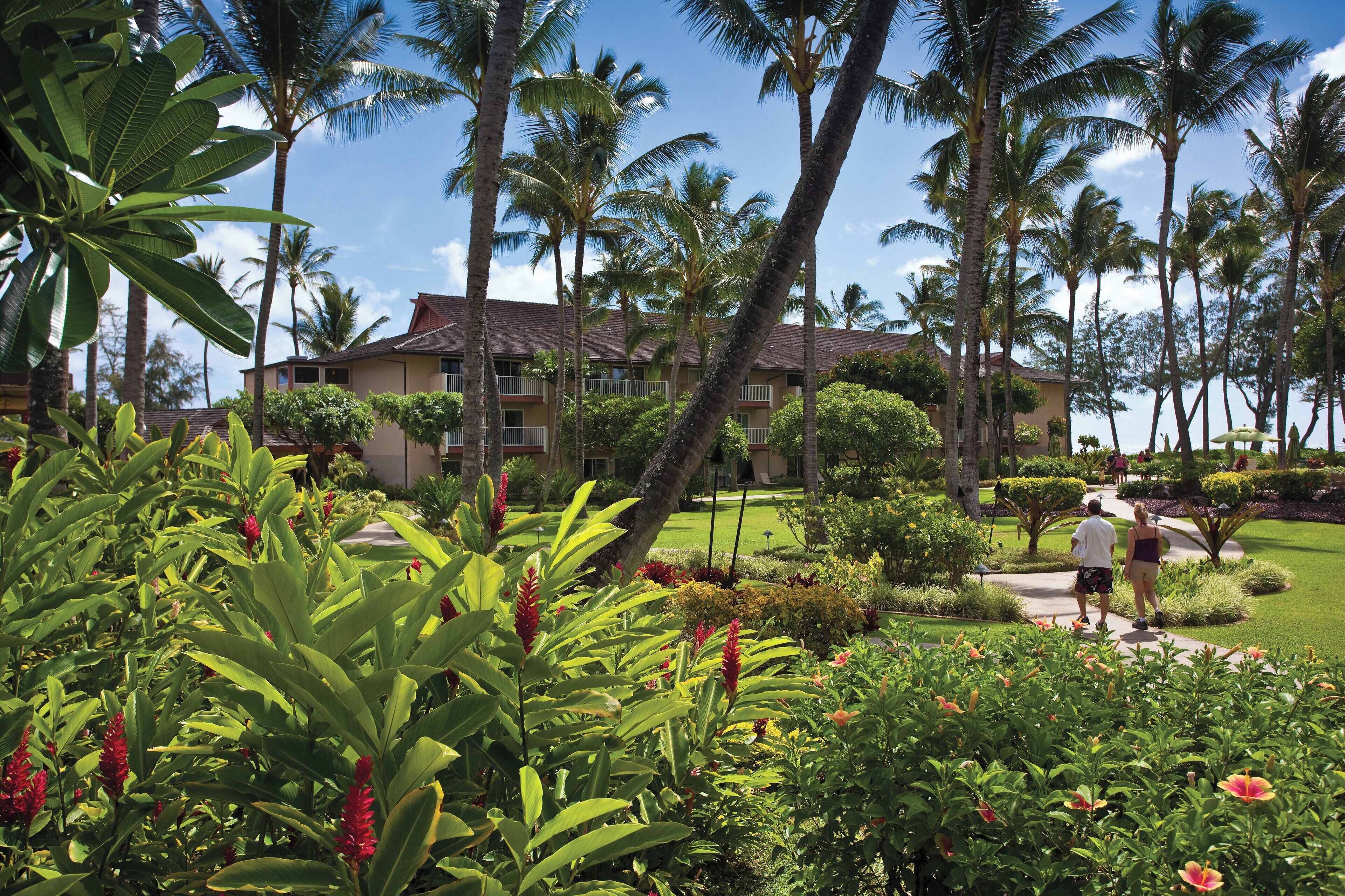 A hotel with a garden, palm trees, and a pathway.