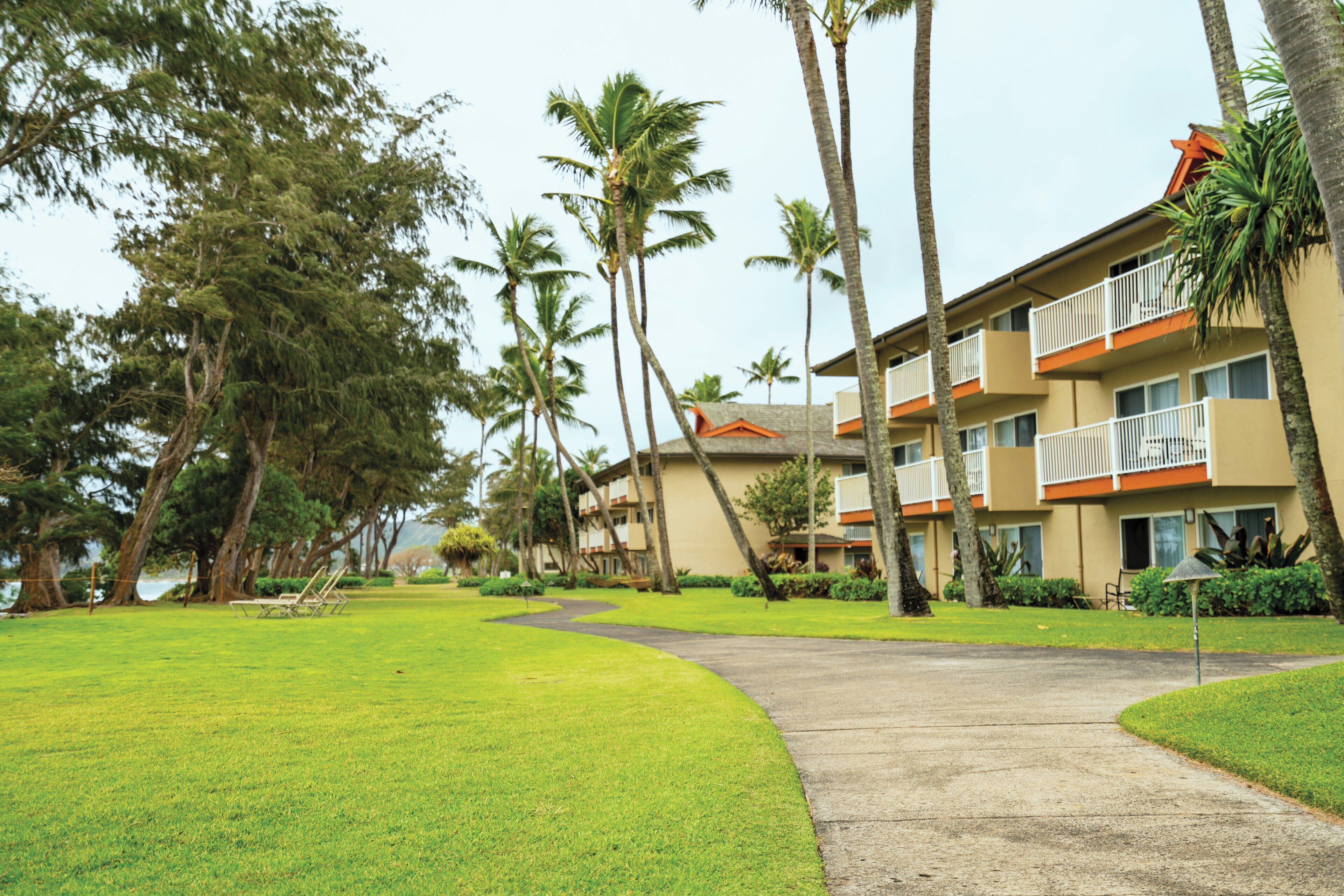 A hotel with a curved pathway, palm trees, and a building with balconies.