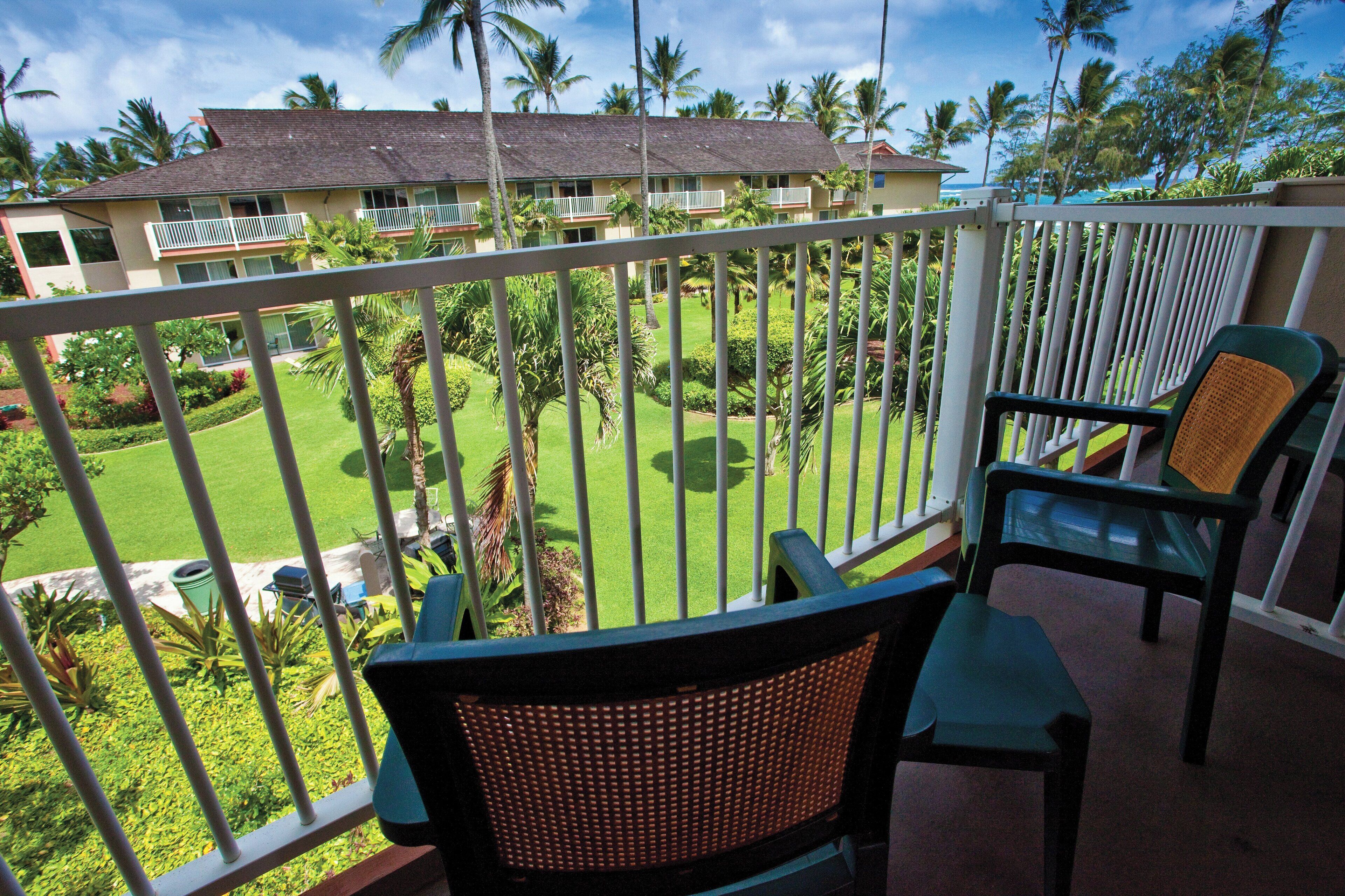 A balcony with two chairs, a view of a well-maintained lawn, and a building with multiple balconies and windows.