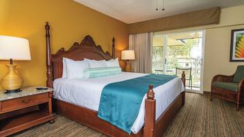 A hotel room with a wooden bed, two bedside tables with lamps, a green throw blanket, and a view of the outdoors through a sliding glass door.