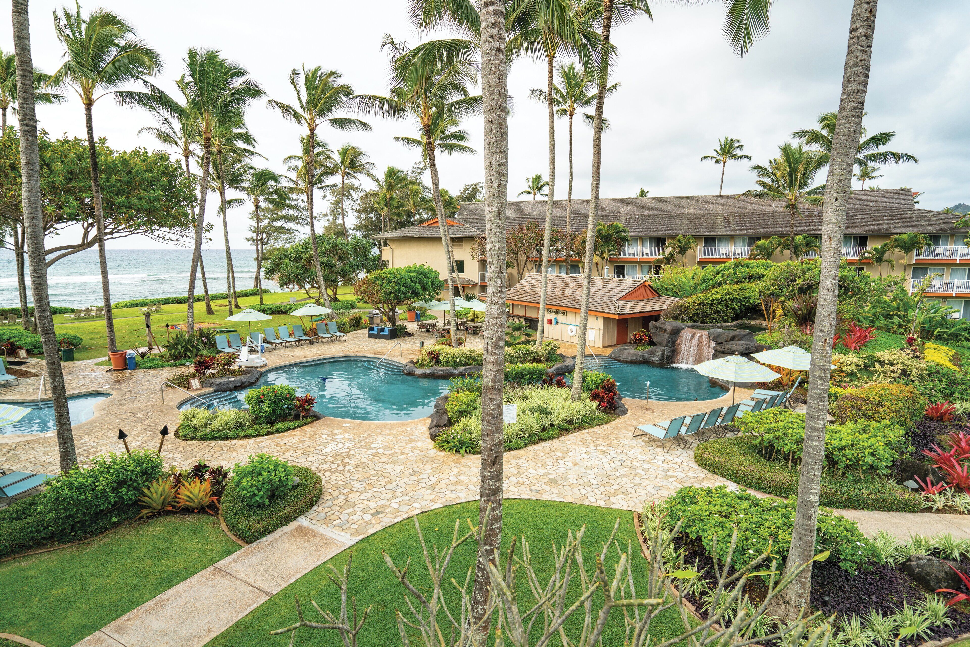 A resort with multiple swimming pools, palm trees, and a view of the ocean.