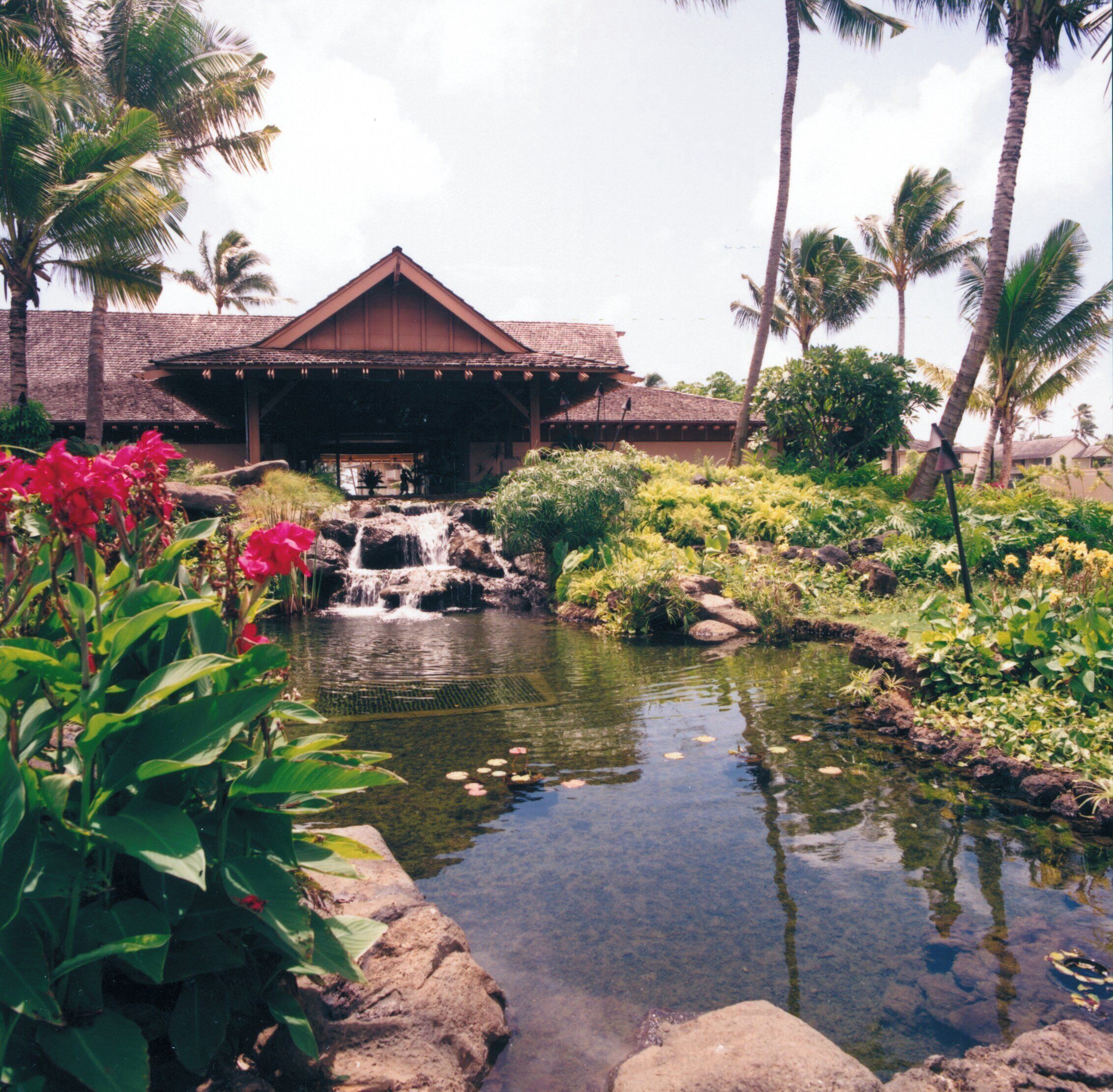 Um resort com uma cascata, vegetação exuberante e um edifício tradicional com telhado de palha.