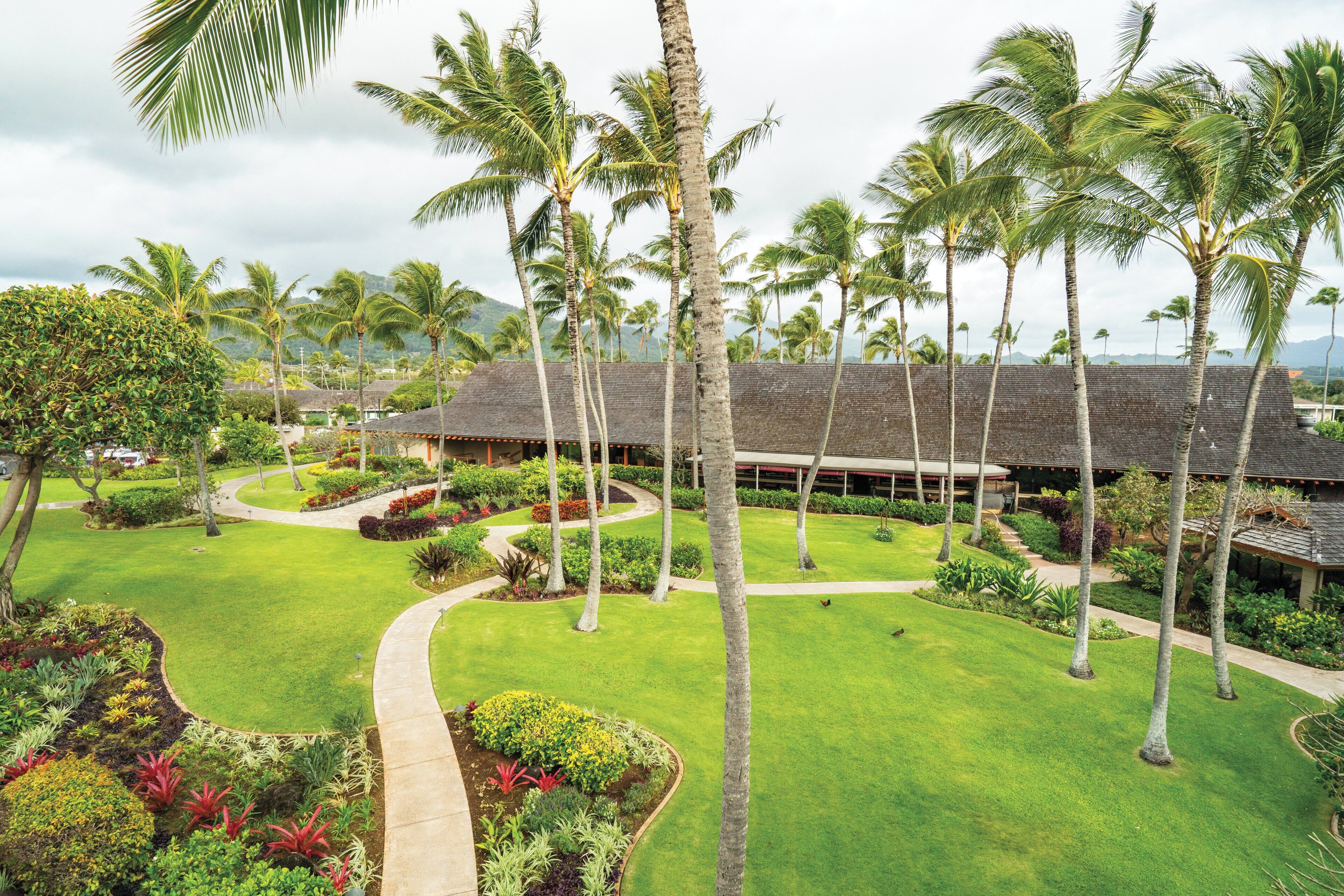 A resort with a central building surrounded by palm trees and well-maintained lawns.