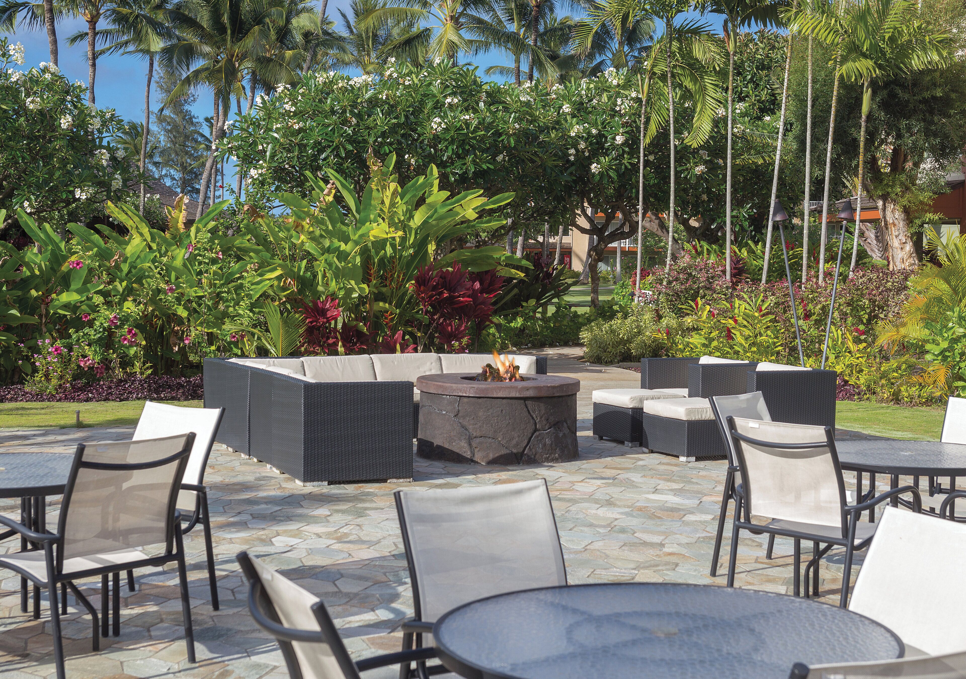 An outdoor patio with stone flooring, wicker furniture, and a central fire pit.
