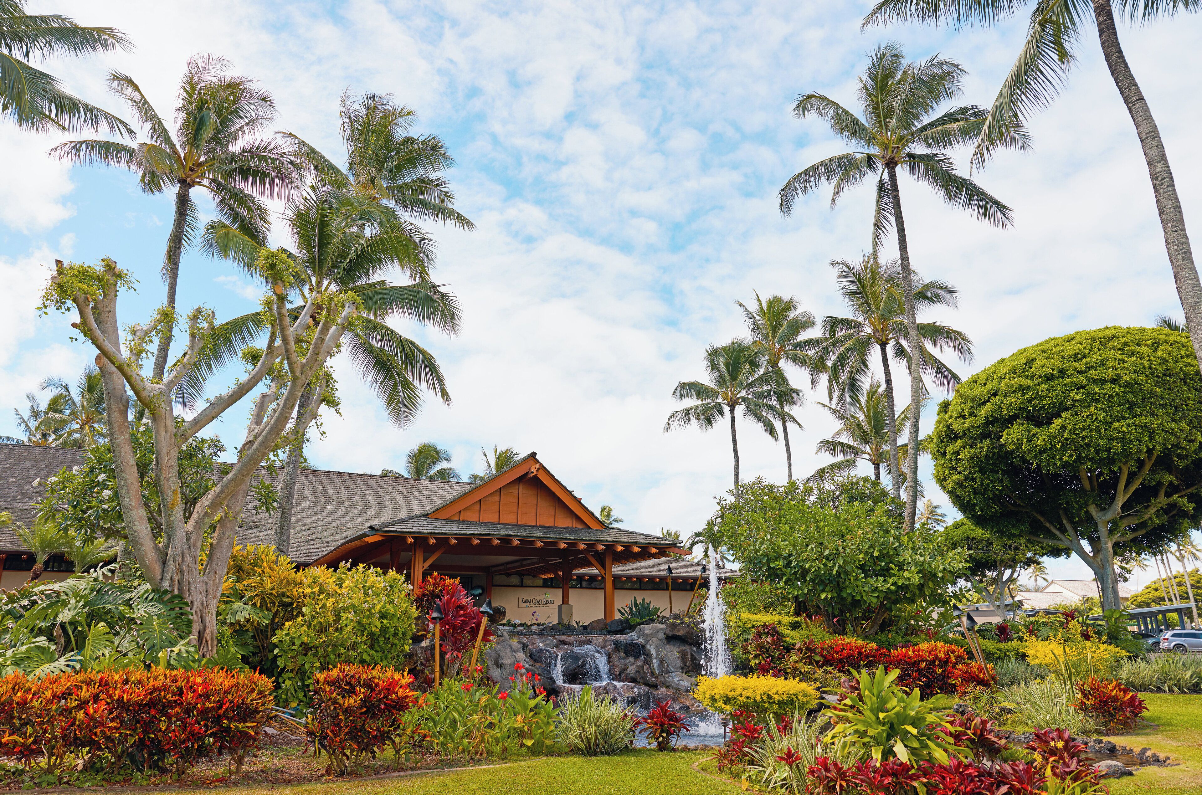 A resort with a covered pavilion, palm trees, a waterfall, and tropical landscaping.