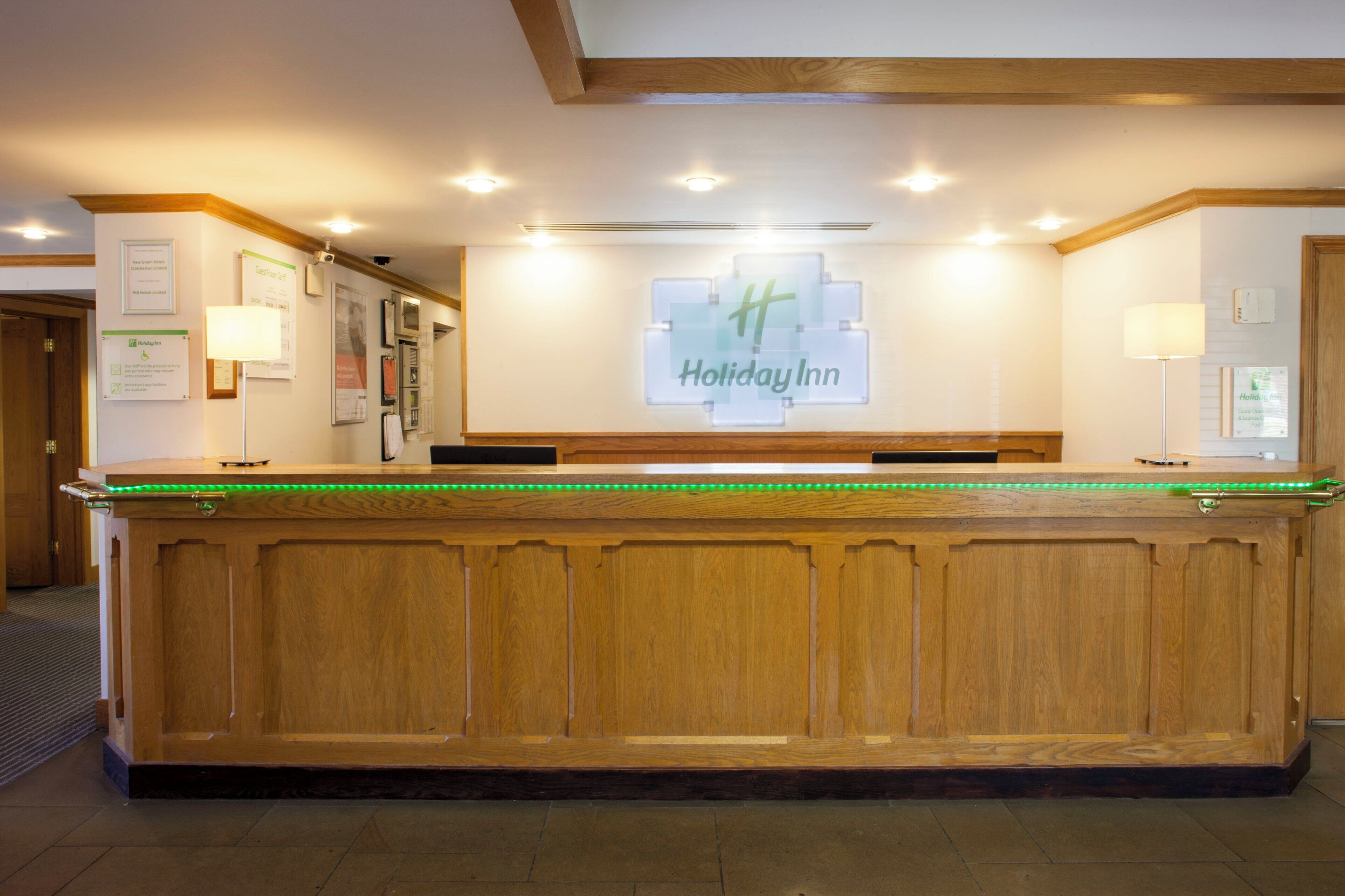 A reception desk with a Holiday Inn sign, wooden paneling, and a green neon light strip.