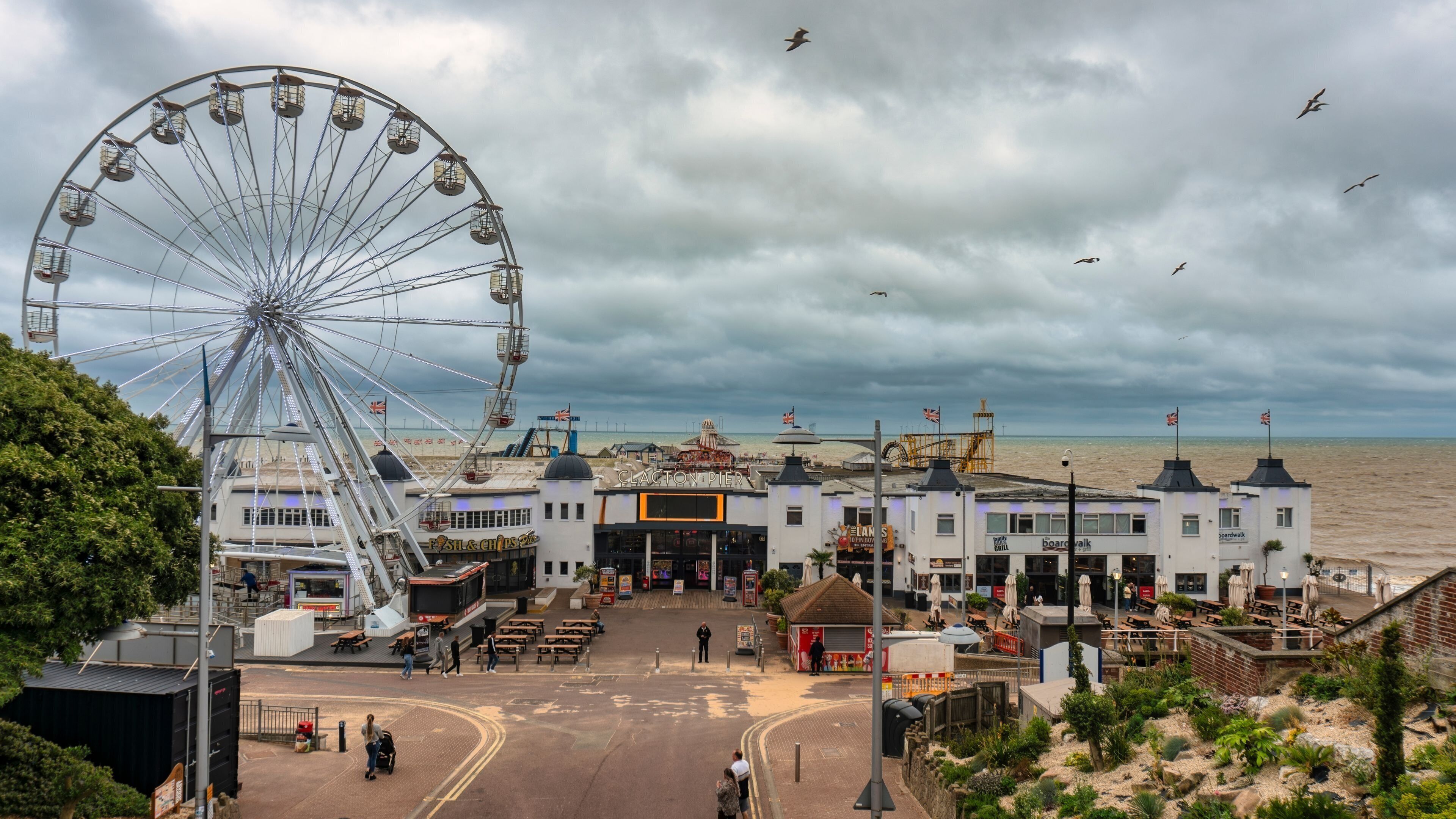 A coastal pier with a large Ferris wheel, a boardwalk, and a beachfront restaurant.