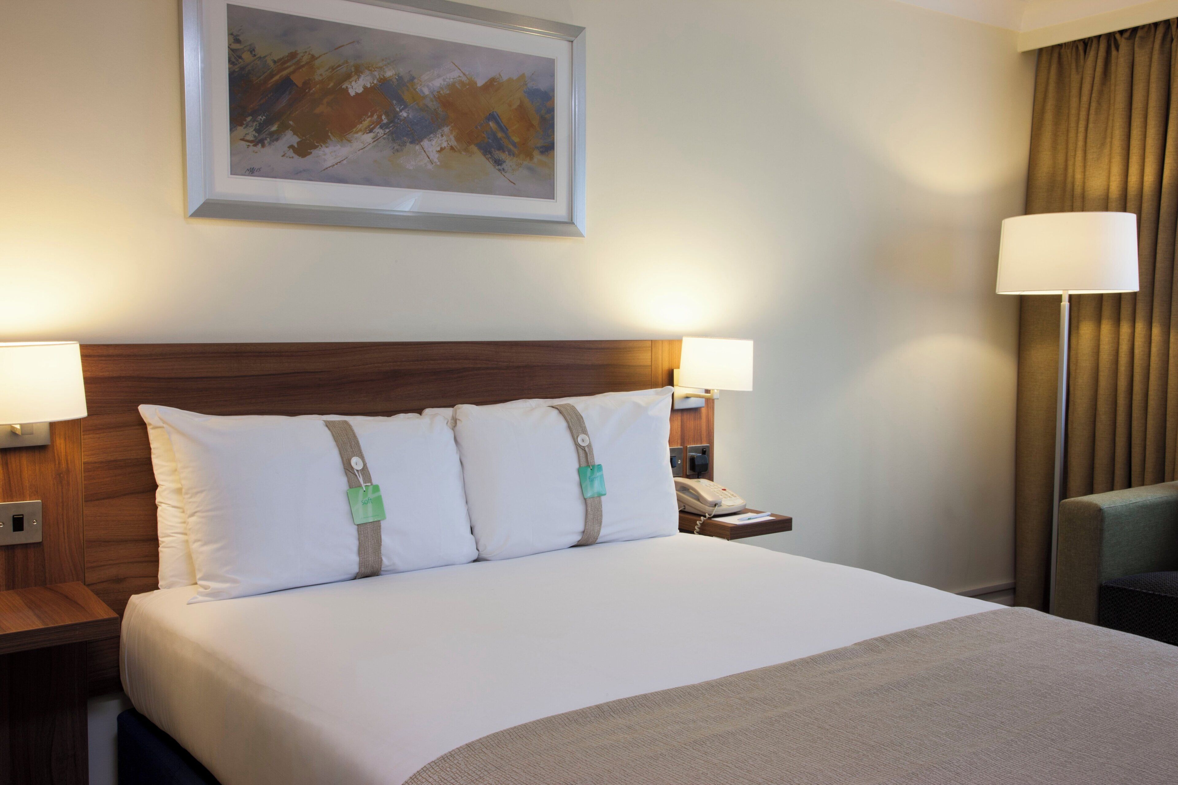Ein Hotelzimmer mit einem großen Bett, zwei Nachttischlampen, einem Telefon und einem Gemälde an der Wand.