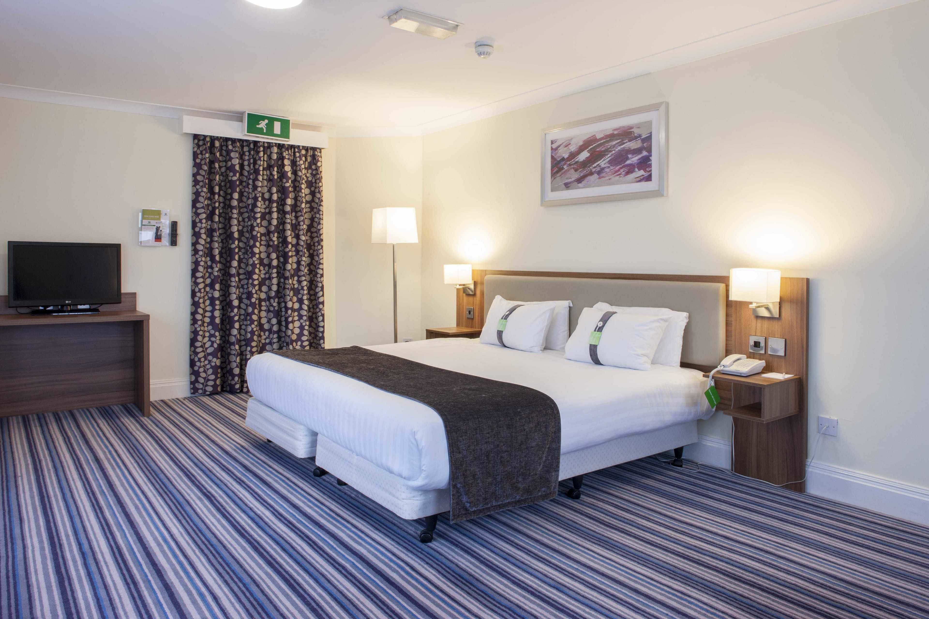 A hotel room with a large bed, a flat-screen TV, a desk, and a telephone.