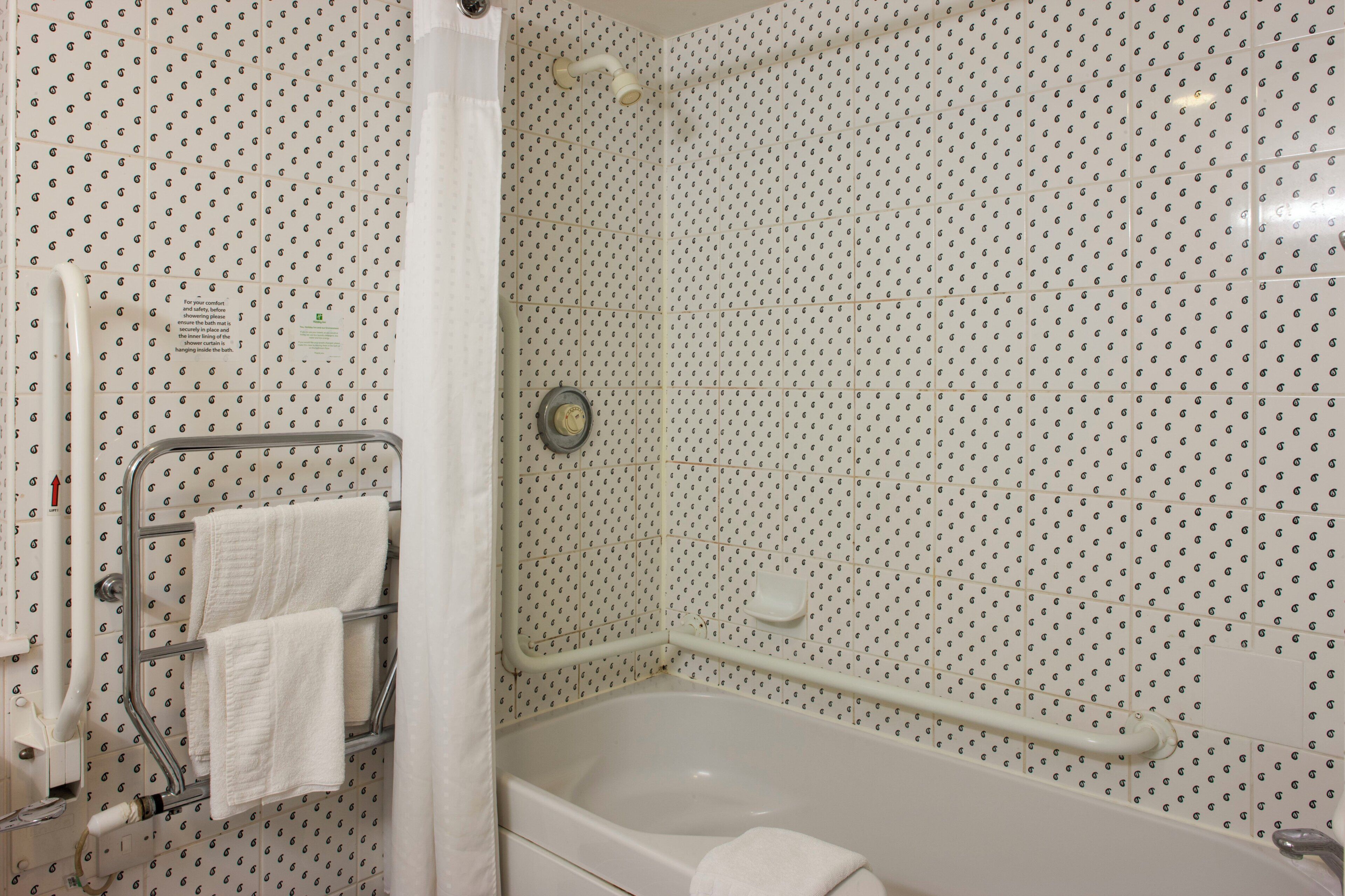 A bathroom with a shower, a bathtub, a towel rack with two towels, and a handrail.