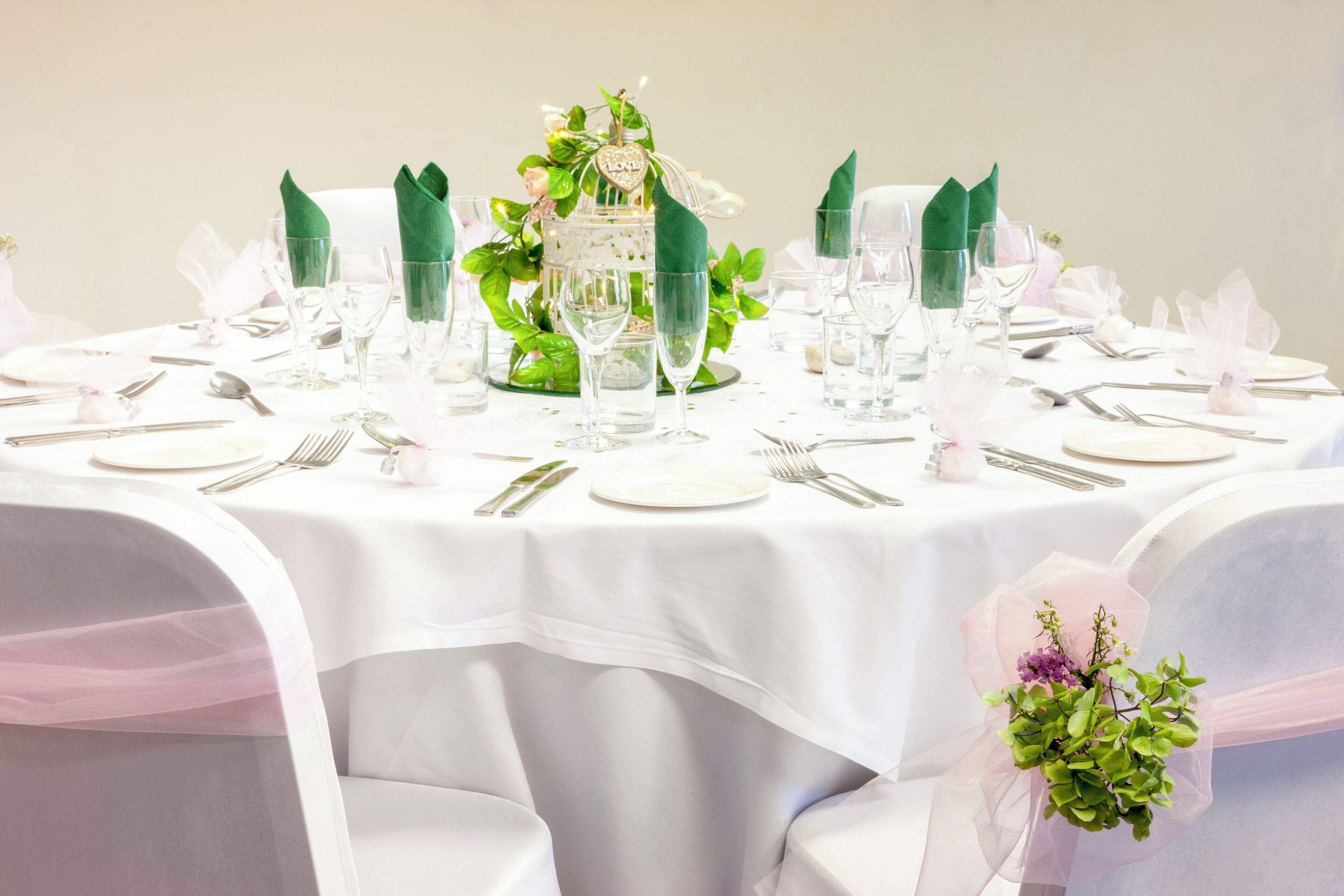 A round table set for a formal event with clear glassware, silverware, and a centerpiece with greenery and a heart-shaped decoration.