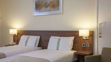A hotel room with two beds, nightstands, a lamp, a chair, and a painting on the wall.