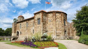 A historic stone building with a flag, a dome, and a garden with colorful flowers. - Holiday Inn Colchester by IHG (Colchester)