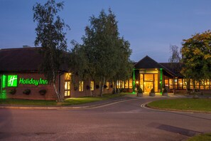 A Holiday Inn hotel with a brick facade, a well-lit entrance, and a parking area. - Holiday Inn Colchester by IHG (Colchester)