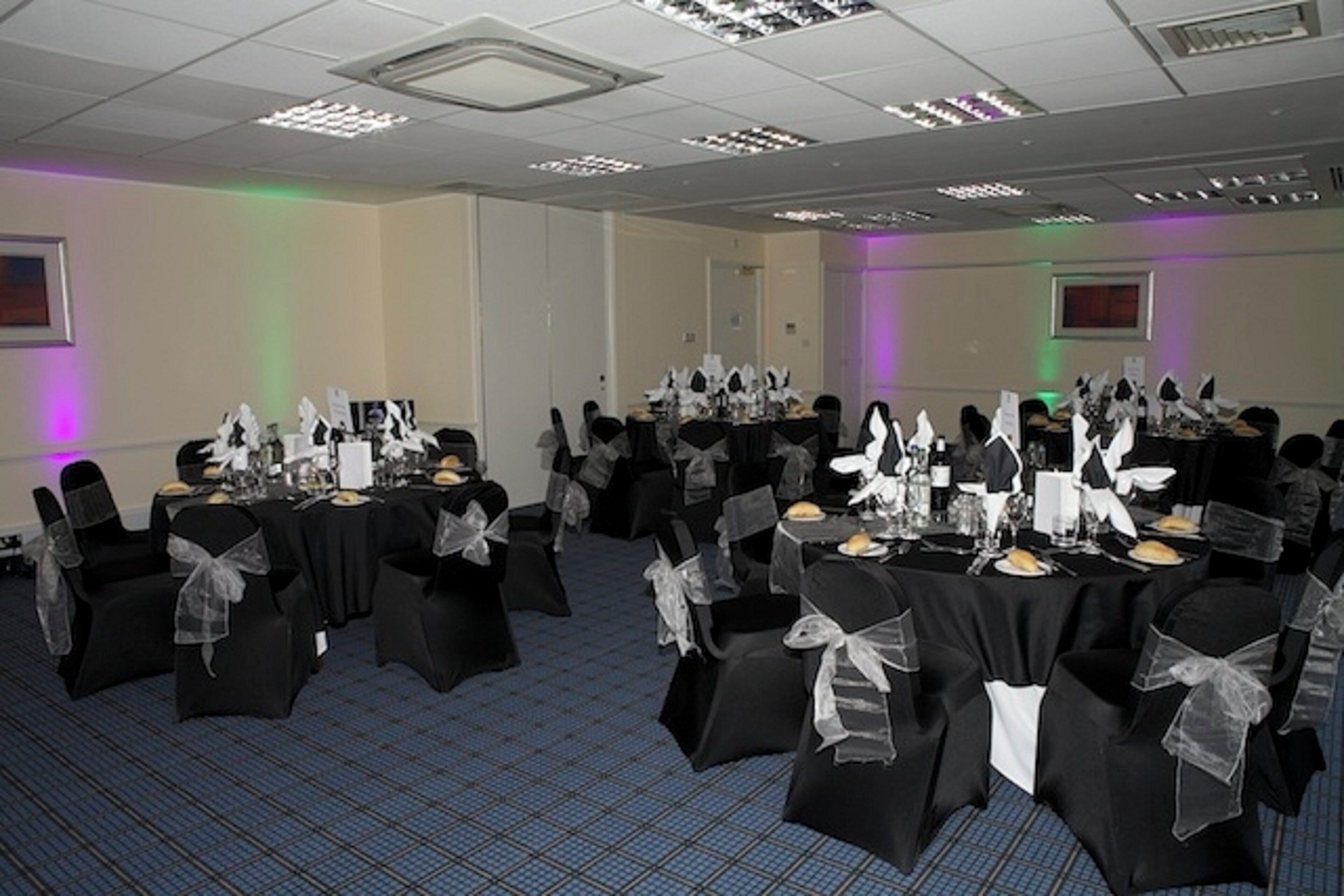A conference room with multiple tables set for a formal event, featuring black tablecloths and chairs with white sashes.