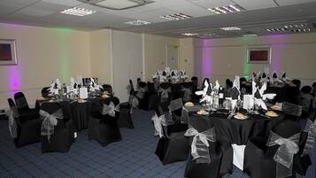A conference room with multiple tables set for a formal event, featuring black tablecloths and chairs with white sashes.