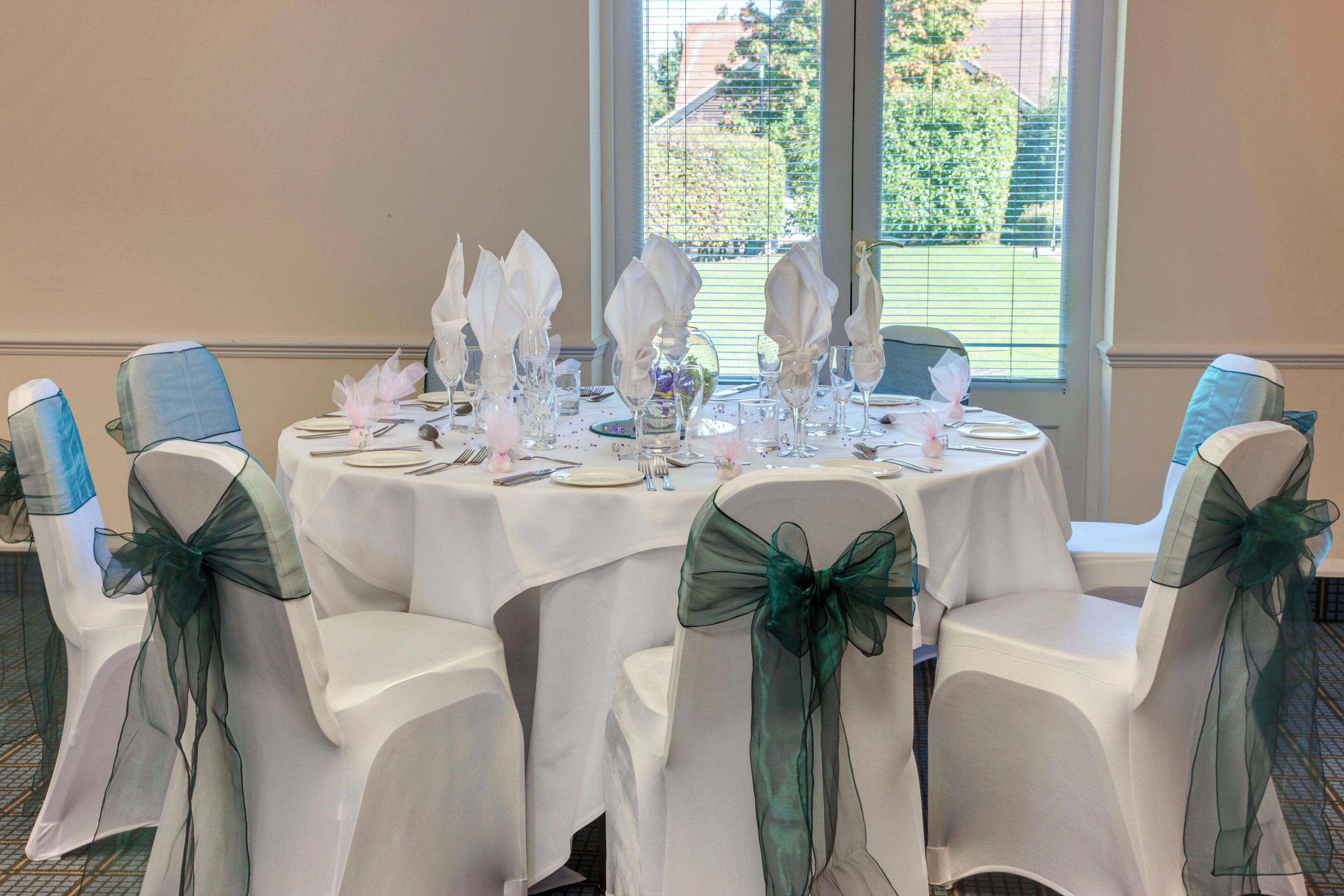 A round table set for a formal event with white tablecloths and chairs adorned with green sashes.